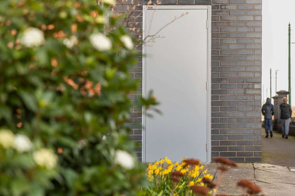 Steel PAS 24 security door partly screened by planting