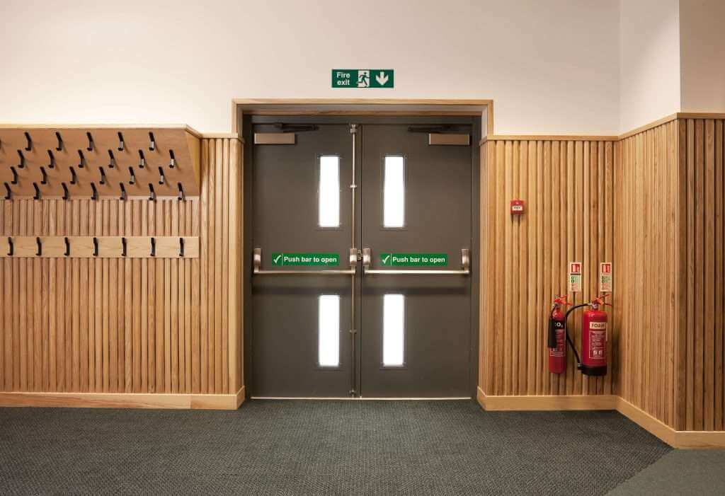 Dark steel doors with panic exit bars in a timber-clad interior