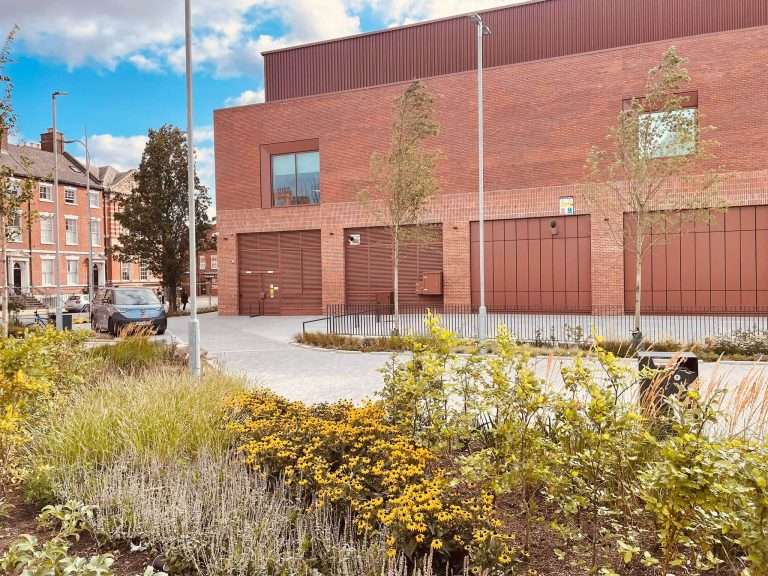 Red brick building with steel roller shutter doors and landscaped entrance