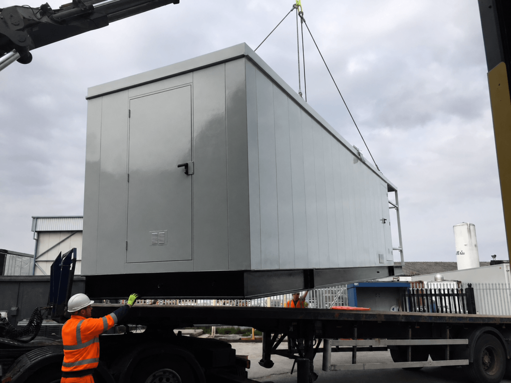 Steel enclosure being loaded onto a flatbed lorry by crane