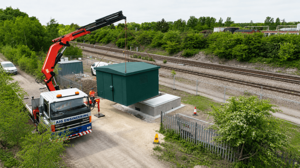 Crane lifting a small steel cabinet near a railway line